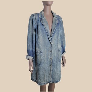 May include: A long, light blue denim jacket with a button-up front and two patch pockets. The jacket has a classic collar and long sleeves.