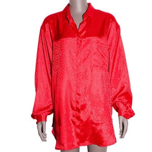 May include: A vibrant red button-down shirt with long sleeves and a chest pocket. The shirt features a subtle, textured pattern throughout the fabric. The collar is open, and the cuffs are buttoned. The shirt is displayed on a mannequin.