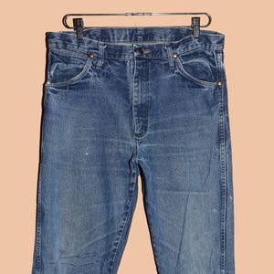 Pu&ograve; includere: Un paio di jeans blu denim con una vestibilit&agrave; classica a gamba dritta. I jeans hanno un lavaggio chiaro e sono leggermente sbiaditi.