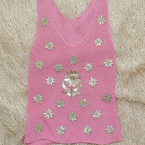 K&ouml;nnte beinhalten: Ein pinkfarbenes Stricktop mit einem Blumendesign. Die Blumen sind aus silbernen Pailletten gefertigt und &uuml;ber die Vorderseite des Tops verteilt.