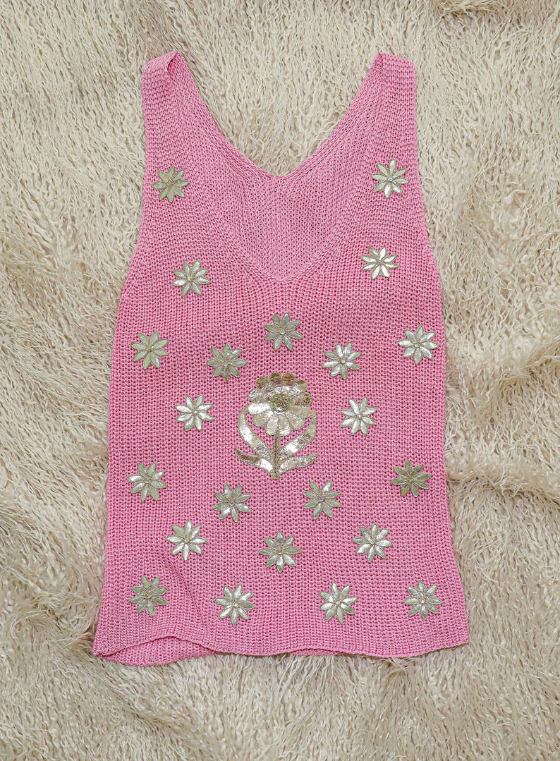 K&ouml;nnte beinhalten: Ein pinkfarbenes Stricktop mit einem Blumendesign. Die Blumen sind aus silbernen Pailletten gefertigt und &uuml;ber die Vorderseite des Tops verteilt.