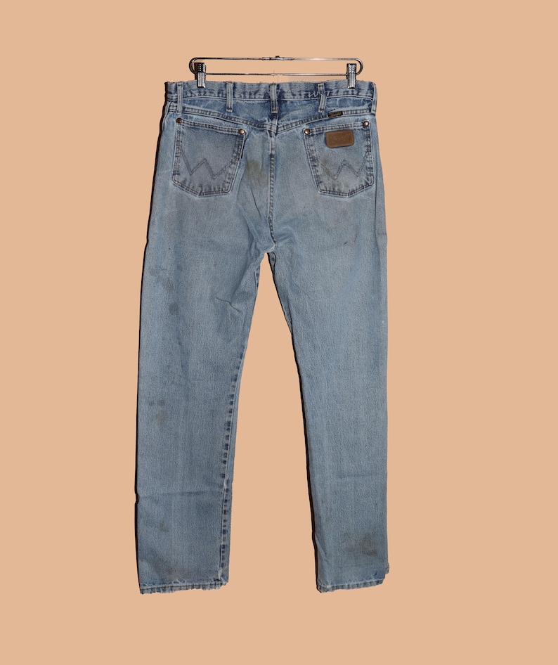 May include: A pair of light blue denim jeans with a brown leather patch on the back pocket. The jeans have a faded look and are worn.