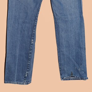 Pu&ograve; includere: Un paio di jeans blu denim a gamba dritta. I jeans hanno un aspetto sbiadito e alcuni segni di usura.