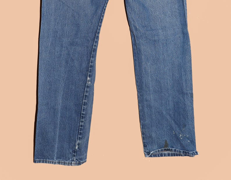 Pu&ograve; includere: Un paio di jeans blu denim a gamba dritta. I jeans hanno un aspetto sbiadito e alcuni segni di usura.