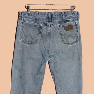 May include: A pair of light blue denim jeans with a brown leather patch on the back pocket that says "Wrangler".