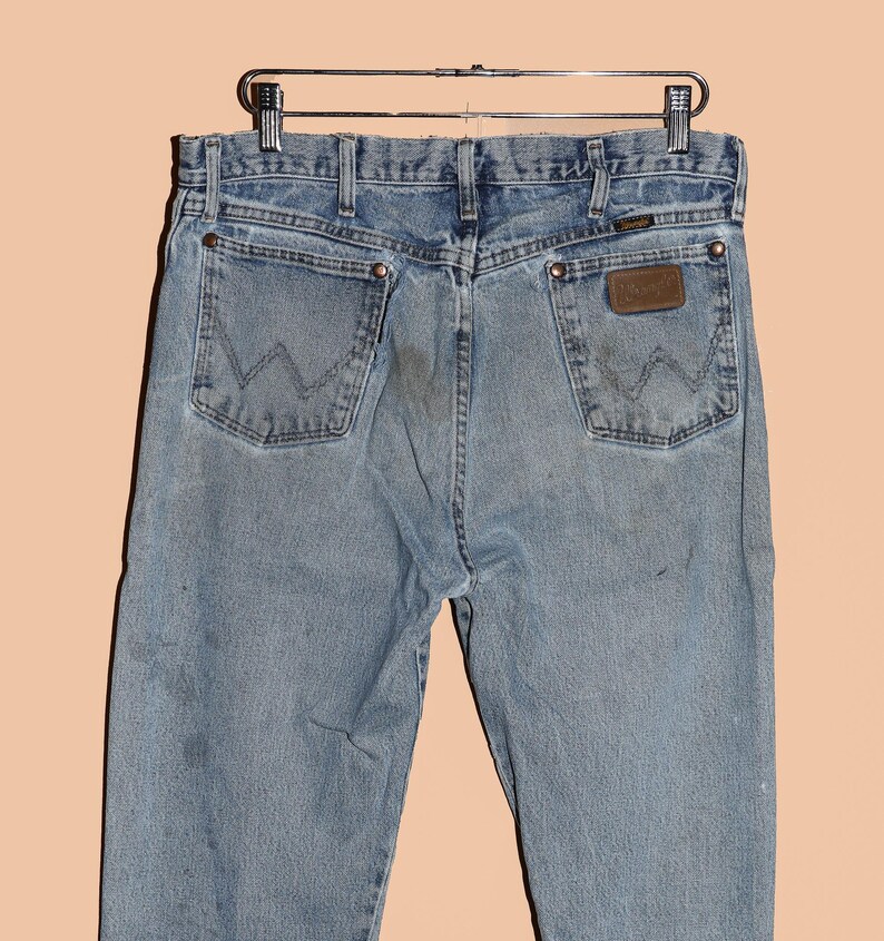 May include: A pair of light blue denim jeans with a brown leather patch on the back pocket that says "Wrangler".