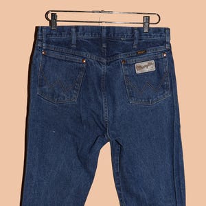 May include: A pair of dark blue denim jeans with a leather Wrangler patch on the back pocket.