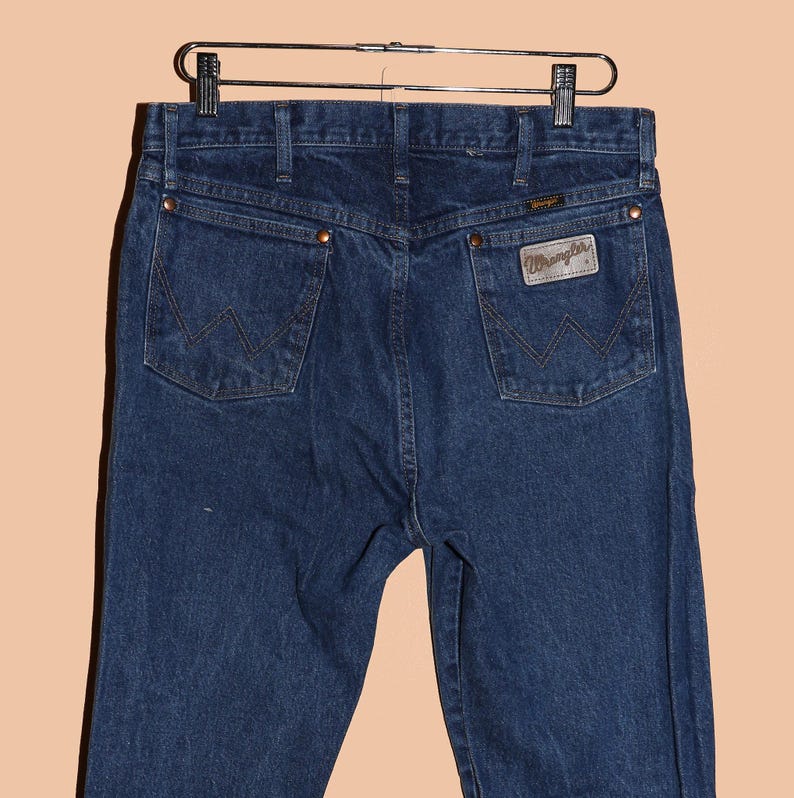 May include: A pair of dark blue denim jeans with a leather Wrangler patch on the back pocket.