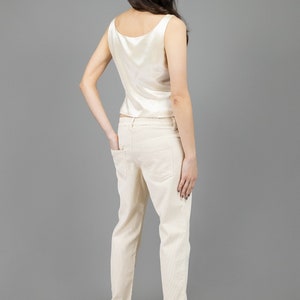 collector of vision model is wearing a size medium cream escada silk corset showing off the back side with scoop neckline, thick straps, styled with cream corduroy pants, nude low pumps