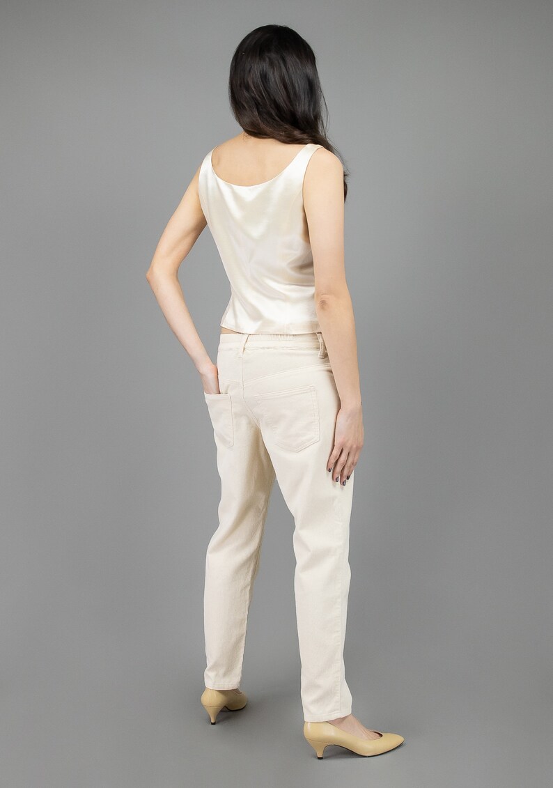 collector of vision model is wearing a size medium cream escada silk corset showing off the back side with scoop neckline, thick straps, styled with cream corduroy pants, nude low pumps