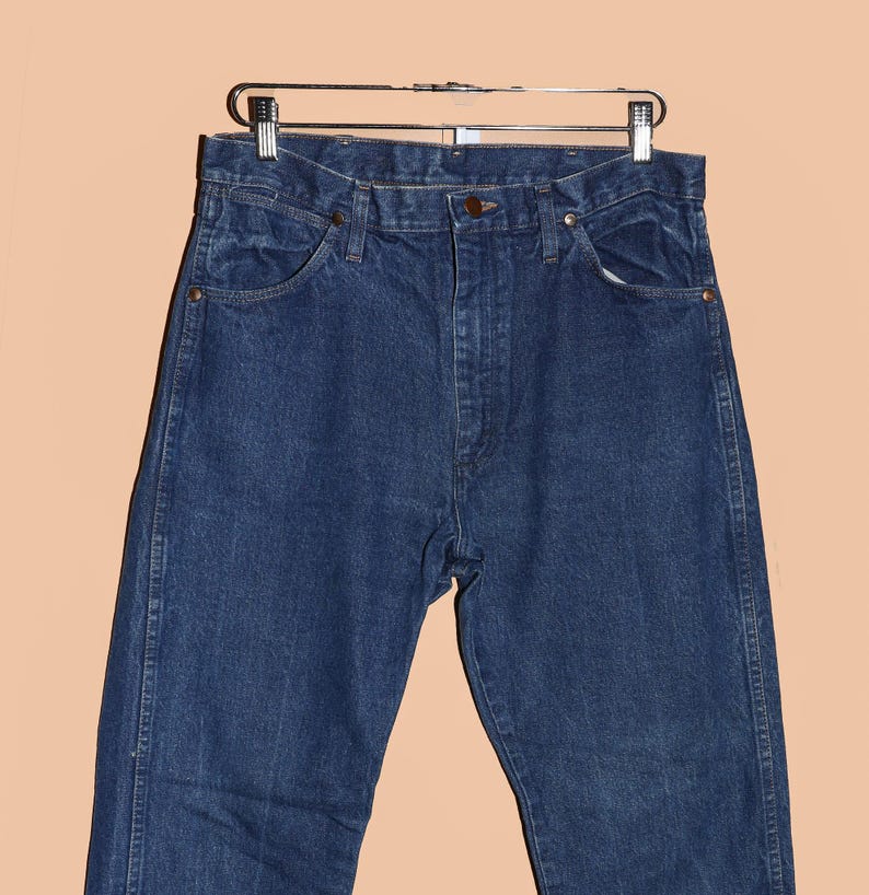 May include: A pair of dark blue denim jeans hanging on a silver hanger. The jeans have a classic five-pocket style and a straight leg.