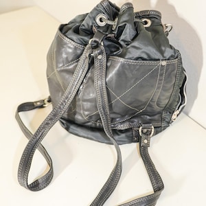 Può includere: Uno zaino nero in pelle e nylon con coulisse e spalline regolabili. Lo zaino ha un design trapuntato e una tasca con cerniera sul davanti.