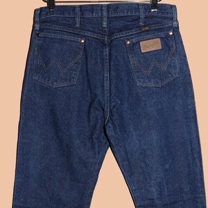 May include: A pair of dark blue denim jeans with a brown leather Wrangler patch on the back pocket.