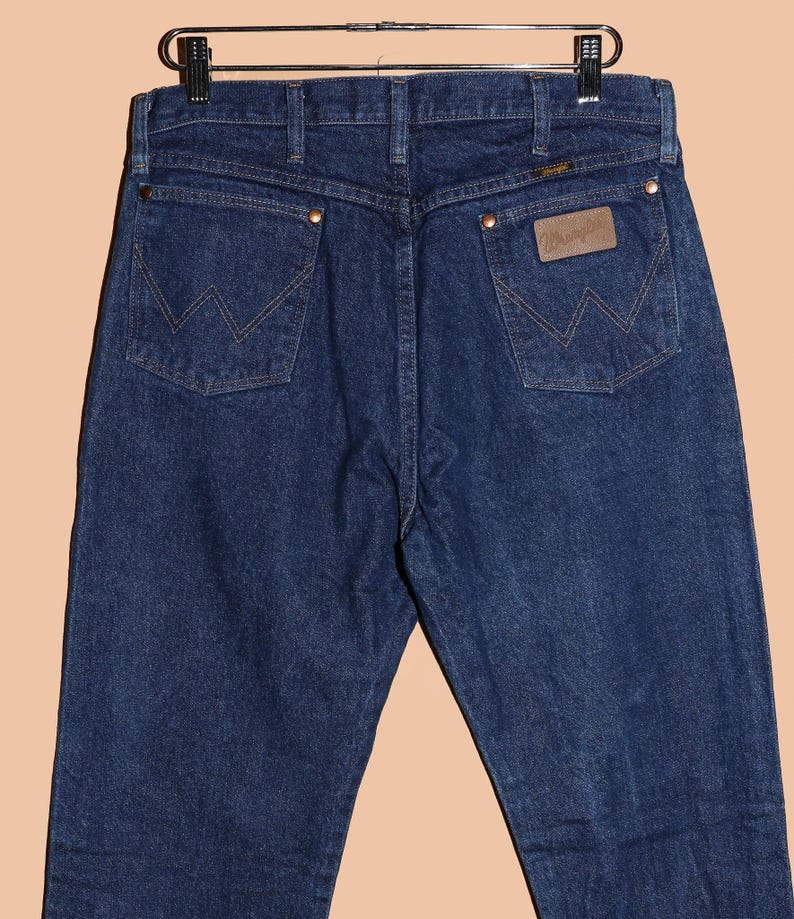 May include: A pair of dark blue denim jeans with a brown leather Wrangler patch on the back pocket.