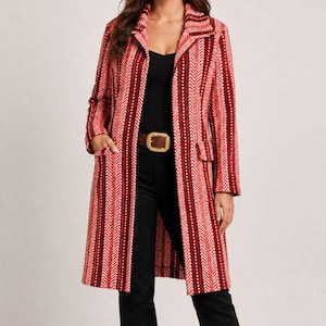 May include: A long-sleeved coat featuring a vertical herringbone pattern in shades of red, dark red, and white. The coat has a notched collar, two front flap pockets, and is worn over a black top and black pants with a brown belt featuring a gold buckle.