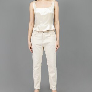 collector of vision model is wearing a size medium cream escada silk corset with square neckline, thick straps, styled with cream corduroy pants, nude low pumps, and crystal dangling earrings