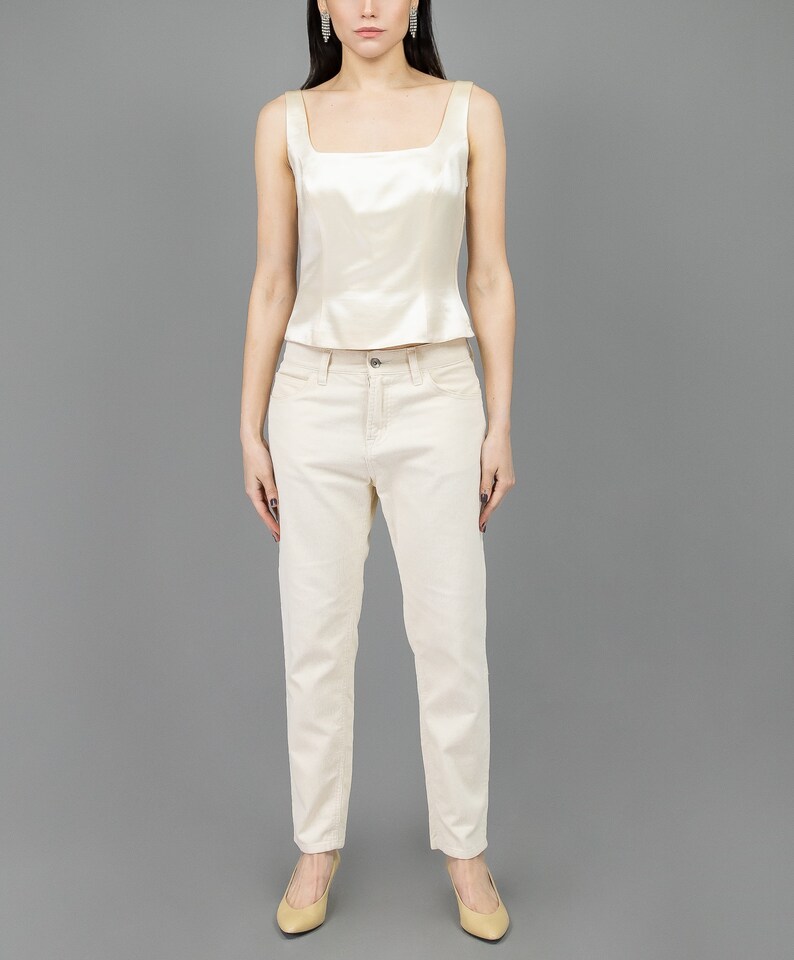 collector of vision model is wearing a size medium cream escada silk corset with square neckline, thick straps, styled with cream corduroy pants, nude low pumps, and crystal dangling earrings