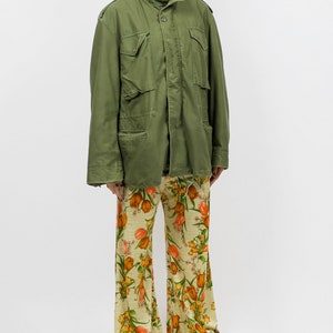 collector of vision model is wearing a size medium 70s wide floral pants showing off the side, styled with green military cargo jacket, white pointed kitten heels, and crystal dangling earrings