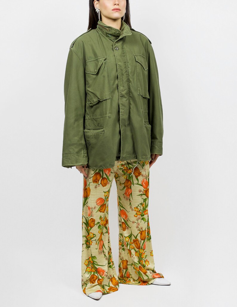 collector of vision model is wearing a size medium 70s wide floral pants showing off the side, styled with green military cargo jacket, white pointed kitten heels, and crystal dangling earrings
