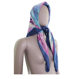 May include: A blue, pink, and white patterned silk scarf with a geometric design. The scarf is tied around a mannequin's head.