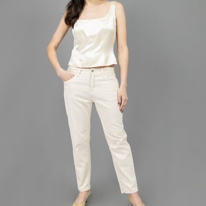 collector of vision model is wearing a size medium cream escada corset with square neckline, thick straps, styled with cream corduroy pants, nude low pumps, and crystal dangling earrings