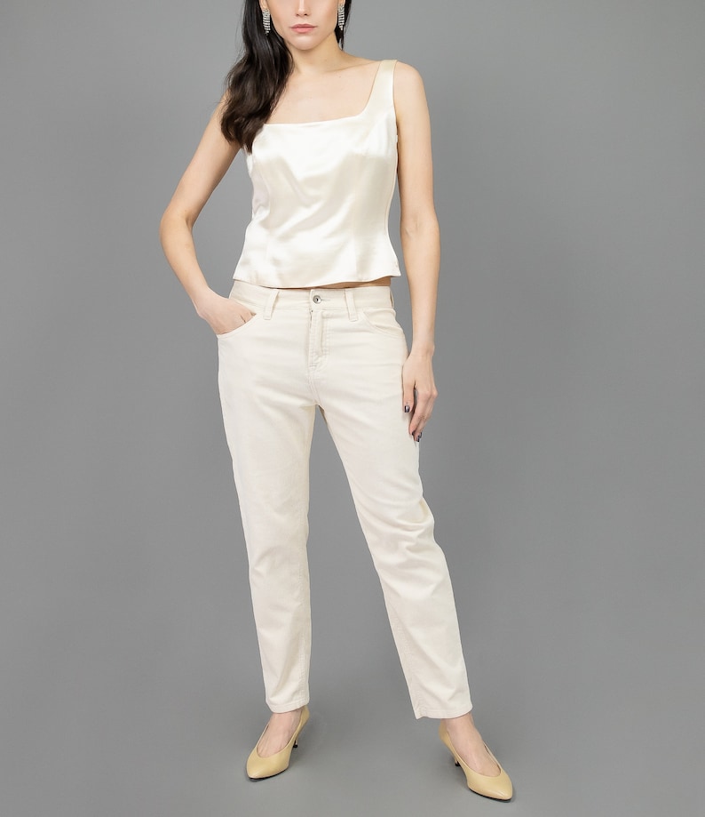 collector of vision model is wearing a size medium cream escada corset with square neckline, thick straps, styled with cream corduroy pants, nude low pumps, and crystal dangling earrings