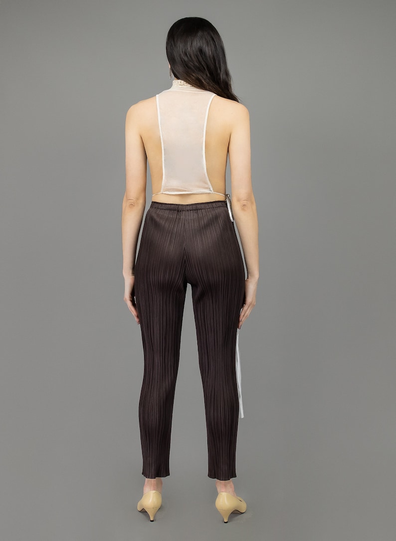 collector of vision model is wearing a size small victorian lace collar vest showing off the back with mesh, adjustable side tie closure, styled with plum issey miyake pleated pants, and nude pumps