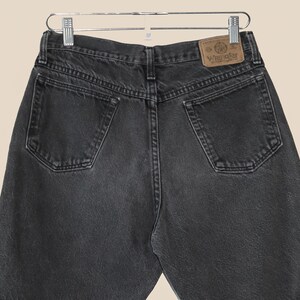 May include: Black denim jeans with a brown leather Wrangler label on the back pocket.