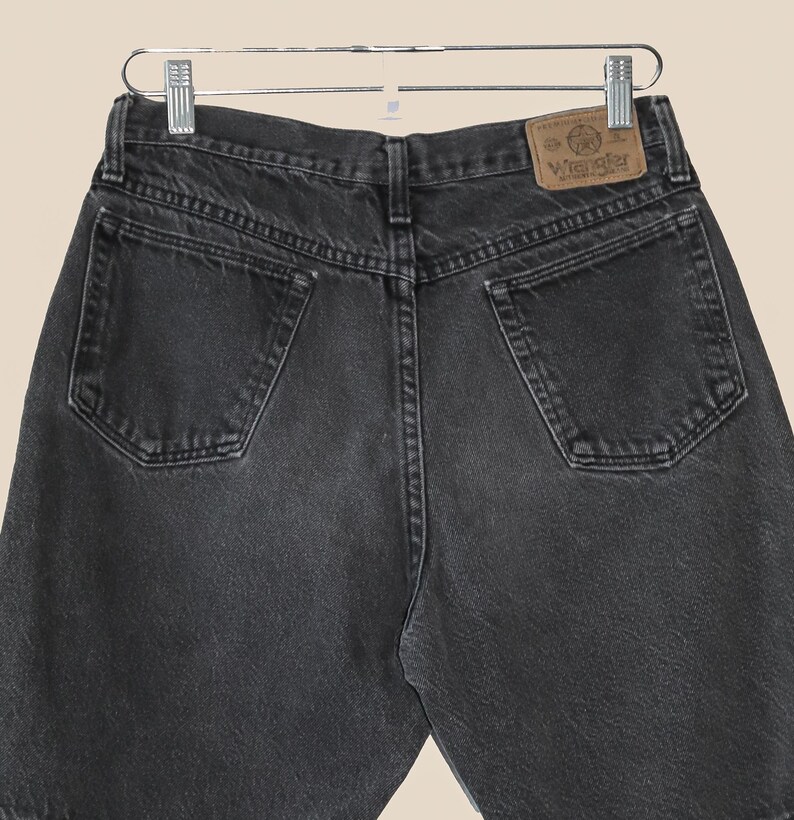 May include: Black denim jeans with a brown leather Wrangler label on the back pocket.