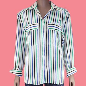 May include: A long-sleeved button-down shirt with vertical stripes in black, blue, and green on a white background. The shirt has two chest pockets and a collared neckline. The cuffs are folded up.