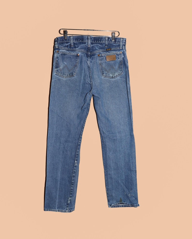 Pu&ograve; includere: Un paio di jeans blu denim con una toppa in pelle marrone sulla tasca posteriore. I jeans hanno una gamba dritta e una vestibilit&agrave; classica.