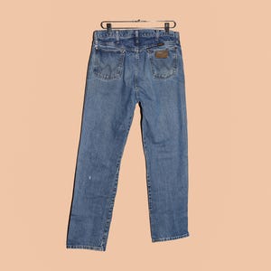 May include: A pair of blue denim jeans with a brown leather patch on the back pocket. The jeans have a classic straight leg fit.