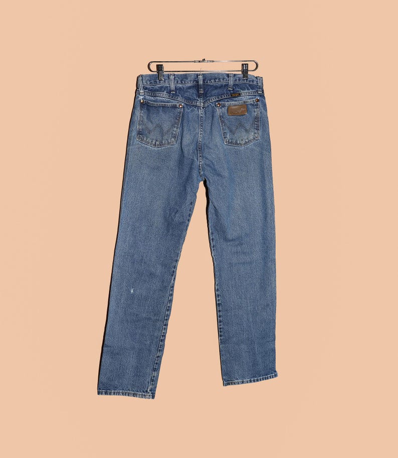 May include: A pair of blue denim jeans with a brown leather patch on the back pocket. The jeans have a classic straight leg fit.