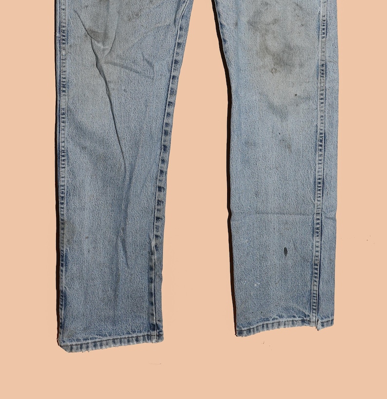 May include: A pair of light blue denim jeans with faded areas and visible stitching. The jeans have a straight leg and a classic fit.
