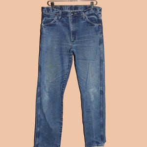 Pu&ograve; includere: Un paio di jeans blu in denim con gamba dritta. I jeans hanno un design classico a cinque tasche e una chiusura con bottoni.