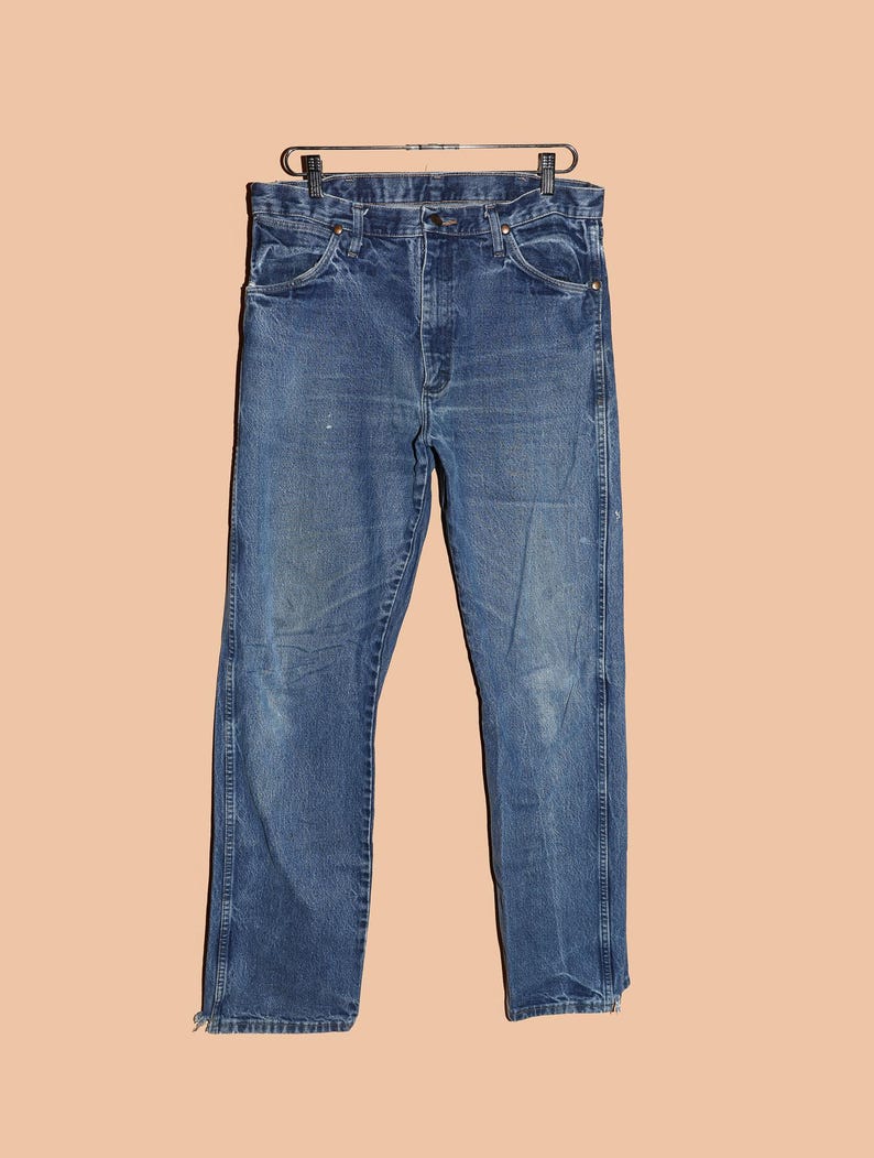 Pu&ograve; includere: Un paio di jeans blu in denim con gamba dritta. I jeans hanno un design classico a cinque tasche e una chiusura con bottoni.