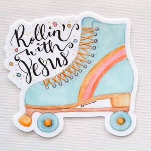 May include: A blue and orange roller skate with rainbow stripes and white laces. The text "Rollin' with Jesus" is written in black cursive on the skate.