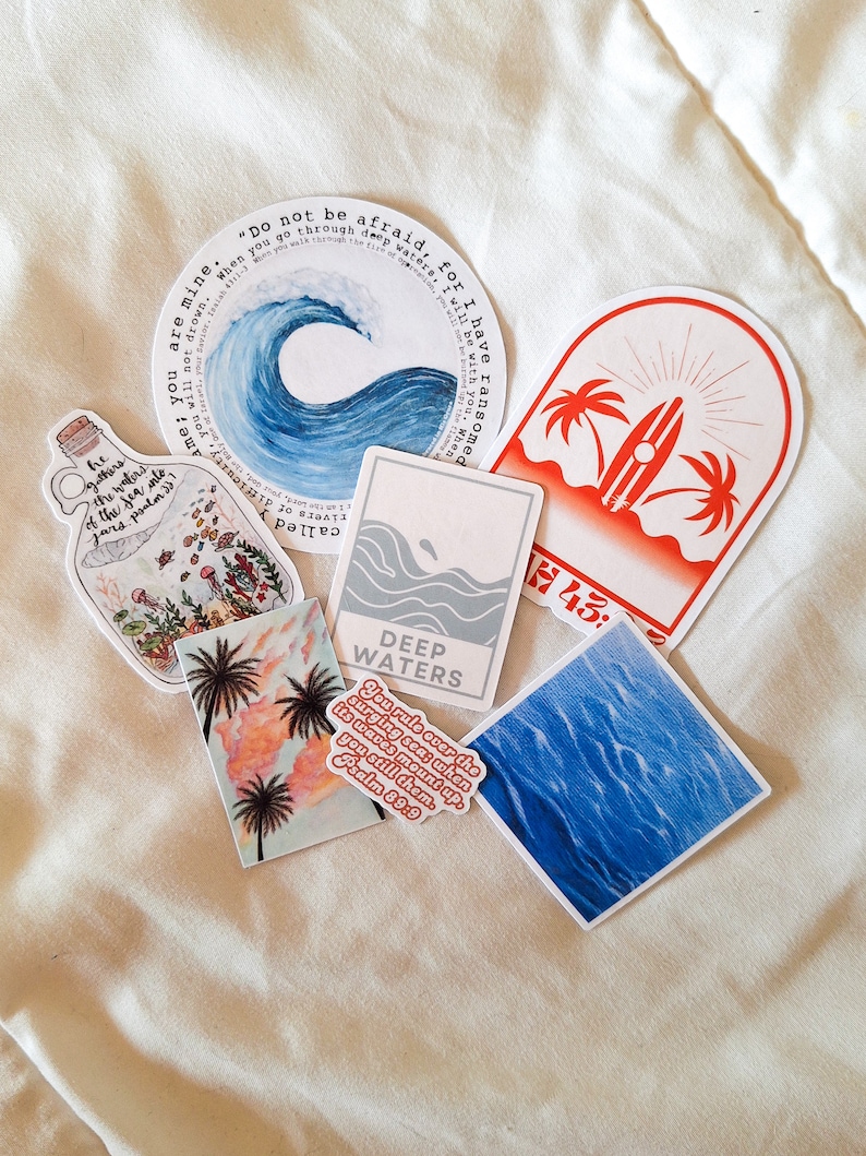 May include: Assortment of stickers featuring ocean and beach themes. Stickers include a blue wave with the text "Do not be afraid, for I have ransomed you. When you go through deep waters, I will be with you, you will not drown. You are mine."  Another sticker features a palm tree and surfboard with the text "H43". A third sticker features a blue ocean wave with the text "DEEP WATERS" and the scripture "You rule over the surging sea; when its waves mount up, you still them. Psalm 89:9".