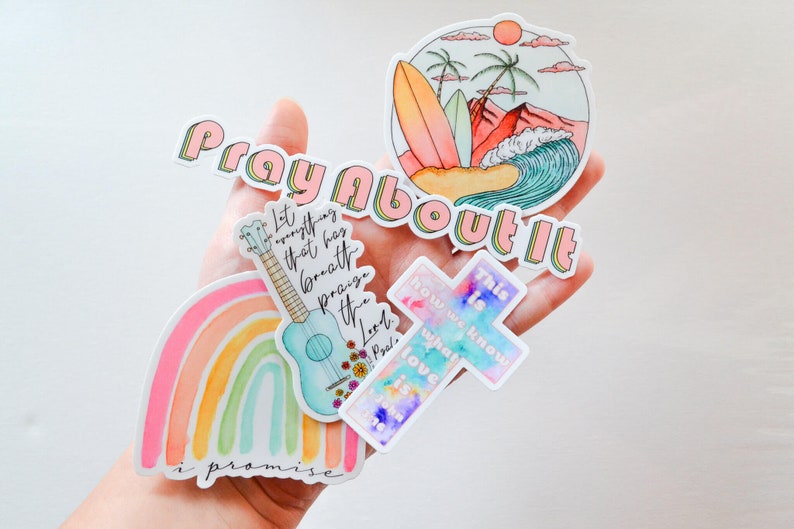 Pode incluir: Um conjunto de cinco adesivos com v&aacute;rios designs e cita&ccedil;&otilde;es inspiradoras. Os adesivos apresentam um arco-&iacute;ris, um ukulele, uma cruz, uma cena de praia e a frase "Ore por isso".