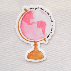 May include: A pink watercolor globe with a gold stand and the text "He's got the whole world in his hands".