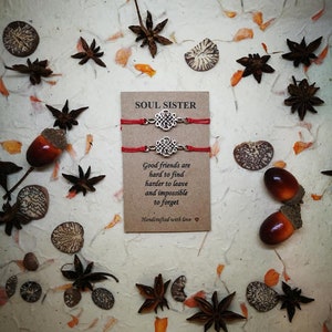 May include: Two red string bracelets with silver charm knots. The card reads "Soul Sister" and "Good friends are hard to find, harder to leave and impossible to forget. Handcrafted with love."