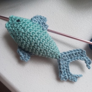 May include: A crocheted teal and blue fish toy. The fish has a small black eye and a long tail.