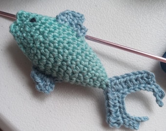 May include: A crocheted teal and blue fish toy. The fish has a small black eye and a long tail.