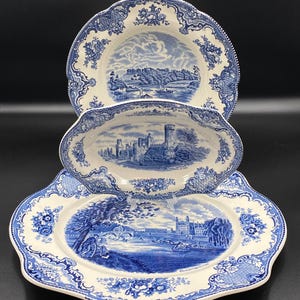 Pode incluir: Conjunto de servir de cerâmica azul e branca de três peças. O conjunto inclui uma travessa grande, uma travessa oval e um prato redondo menor. Cada peça apresenta uma cena de paisagem azul detalhada e uma borda floral.