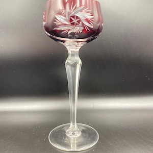 Può includere: Un calice da vino rosso rubino con stelo e base trasparenti e sfaccettati. La coppa presenta un motivo inciso di foglie e un motivo a stella. Il bicchiere è di cristallo. Altezza circa 18 cm.