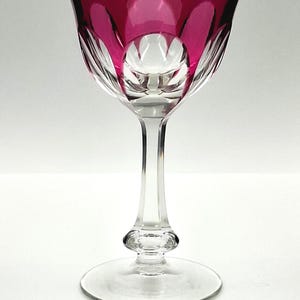 Puede incluir: Una copa de vino transparente con borde fucsia y diseño decorativo de cristal tallado. El tallo es largo y delgado, con base redondeada y pie circular. La copa mide aproximadamente 18 cm de altura.