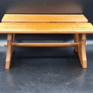 May include: Two small, light brown wooden benches. Each bench has a rectangular top and four legs connected by a horizontal support. The benches are made of a light-coloured wood and have a simple, rustic design. The benches are likely for decorative purposes.