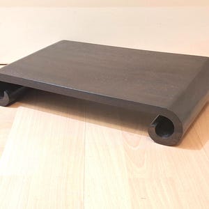 May include: A dark brown, rectangular wooden table with a unique scroll design on each end. The table has a smooth, matte finish and sits on a light-colored wooden floor. The table's dimensions are approximately 36 inches long and 18 inches wide.