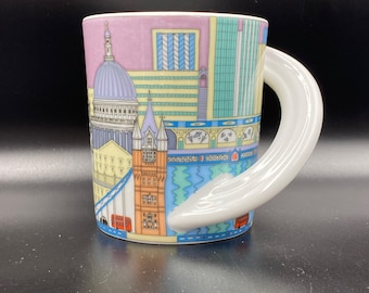 May include: A ceramic mug featuring a London cityscape design. The mug has a white, curved handle and a colorful wrap-around illustration of iconic landmarks, including St. Paul's Cathedral and Tower Bridge. The mug is approximately 4 inches tall.