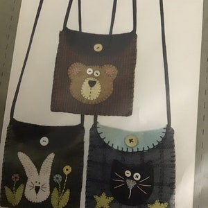 May include: Three small felt bags with different animal faces. The bags are brown, black, and blue with a plaid pattern. Each bag has a button closure and a long strap.